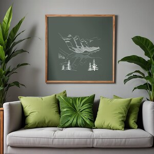 May include: A framed print with a white line drawing of mountains and trees on a dark green backdrop. The print hangs above a grey sofa with green cushions, one with a leaf pattern. Potted plants are positioned on either side of the sofa.