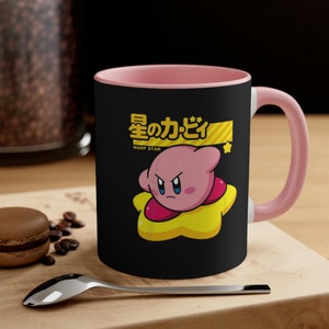 May include: A pink and black ceramic mug with a cartoon character on a yellow star. The character is pink with a grumpy expression and the text "星のカービィ" and "WARP STAR" are printed on the mug.