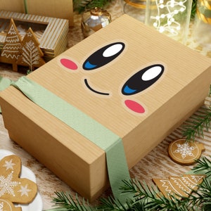 Puede incluir: Una caja de regalo de cartón marrón con una cinta verde. La caja tiene una cara de dibujos animados con una boca sonriente, ojos negros grandes y mejillas rosadas.