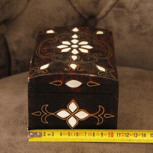 May include: A small wooden box with a dark brown finish and intricate white and gold inlay designs. The box is approximately 10 inches long.