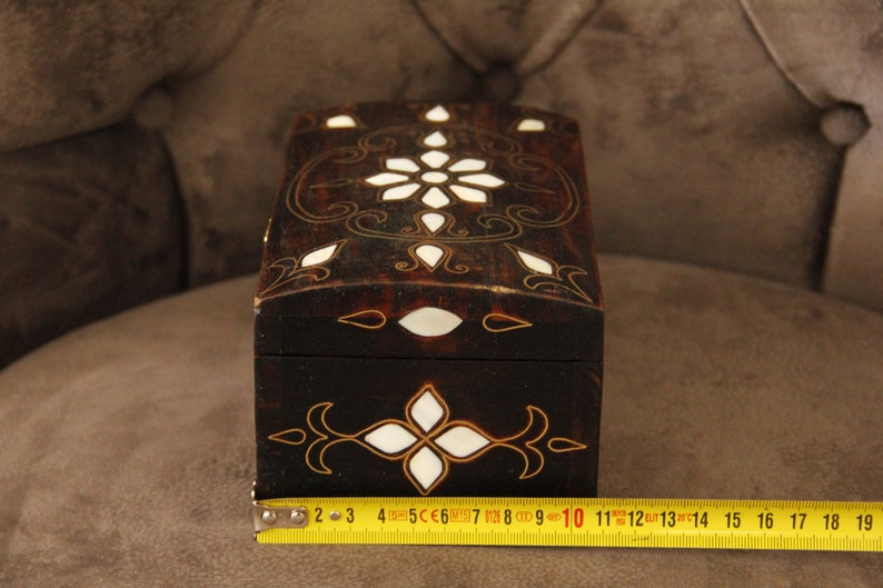 May include: A small wooden box with a dark brown finish and intricate white and gold inlay designs. The box is approximately 10 inches long.