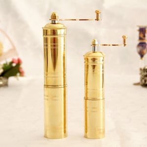 May include: Two gold manual coffee grinders with a crank handle. The grinders are made of brass and have a cylindrical shape. The larger grinder is on the left and the smaller grinder is on the right.