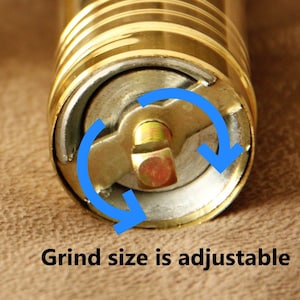 May include: Close-up of a gold pepper grinder with a visible adjustment mechanism. The grind size is adjustable by turning the knob on the side of the grinder.  "Grind size is adjustable" is printed on the bottom of the image.