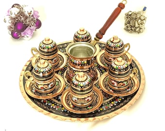 May include: A copper coffee set with a black and floral design. The set includes a coffee pot, six cups with saucers, and a serving tray. The cups and pot have decorative lids. The handle of the coffee pot is made of wood.