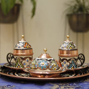Pode incluir: Uma bandeja de servir de cobre com tr&ecirc;s pequenas x&iacute;caras de cobre com tampas. As x&iacute;caras s&atilde;o decoradas com padr&otilde;es florais coloridos. A bandeja tem uma al&ccedil;a de cada lado.