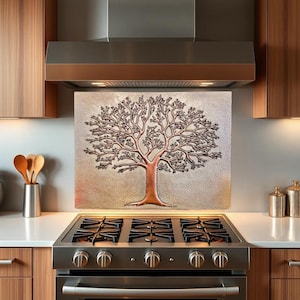 May include: A copper-colored metal backsplash with an embossed tree design. The backsplash is installed above a stainless steel stove with a black cooktop.