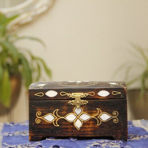 May include: A dark wooden box with a decorative inlay of white and gold. The box has a brass latch and is closed.