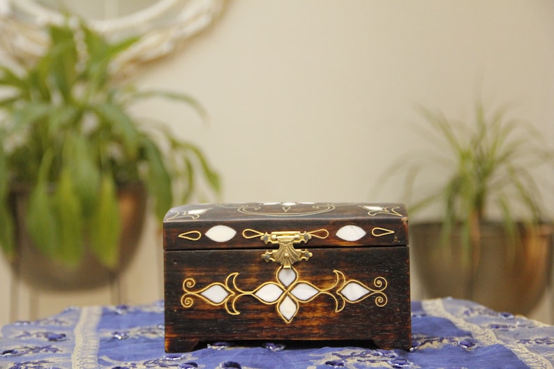May include: A dark wooden box with a decorative inlay of white and gold. The box has a brass latch and is closed.