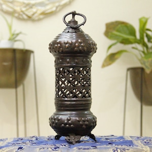 May include: A dark bronze metal lantern with a decorative design. The lantern has a cylindrical shape with a lattice pattern in the center and a ring at the top. The lantern is approximately 12 inches tall.