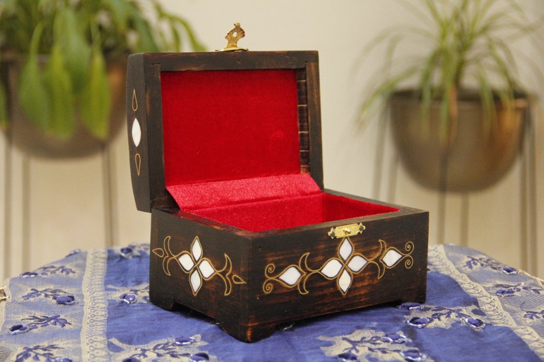 May include: A wooden box with a red velvet interior and intricate white and gold inlay. The box is open and has a brass latch.