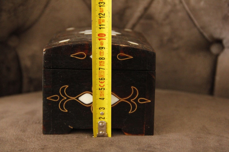 May include: A black wooden box with white and gold inlay. The box is 7 inches long and has a hinged lid.