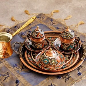 Pode incluir: Uma bandeja de servir de cobre com tr&ecirc;s x&iacute;caras de caf&eacute; de cobre ornamentadas e um cremer a condizer. A bandeja e as x&iacute;caras s&atilde;o decoradas com padr&otilde;es florais coloridos.
