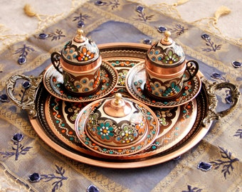 May include: A set of three copper coffee cups with lids and saucers, decorated with colorful floral patterns. The cups are arranged on a copper tray with a decorative border.