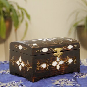 May include: A dark wooden box with a hinged lid and a brass latch. The box is decorated with white inlays and gold accents in a floral pattern.
