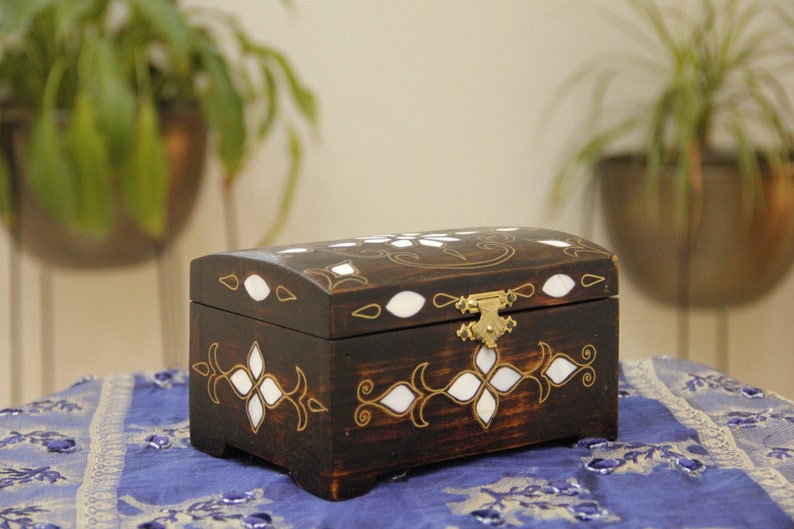 May include: A dark wooden box with a hinged lid and a brass latch. The box is decorated with white inlays and gold accents in a floral pattern.