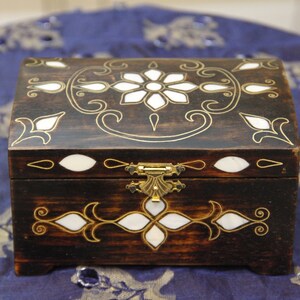 May include: A dark wooden box with a hinged lid and a brass latch. The box is decorated with intricate floral patterns and white mother-of-pearl inlays.