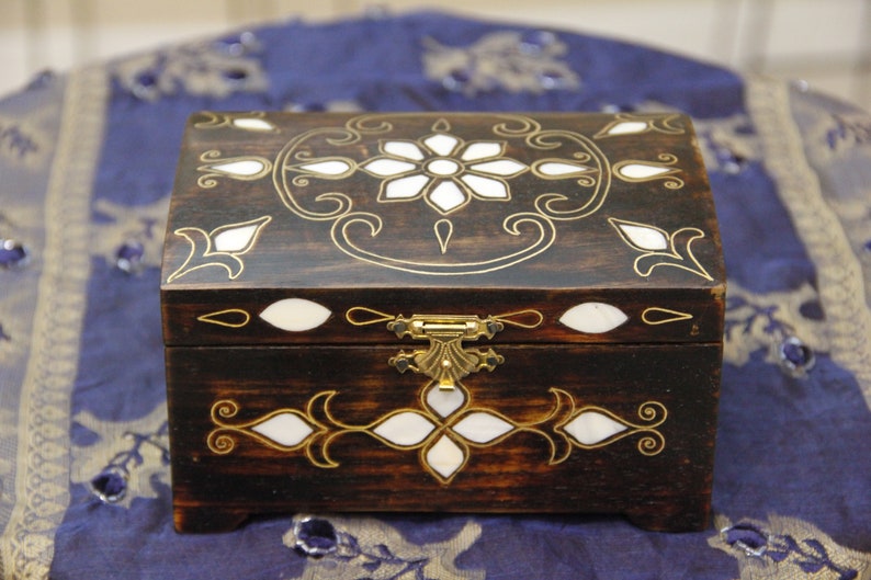 May include: A dark wooden box with a hinged lid and a brass latch. The box is decorated with intricate floral patterns and white mother-of-pearl inlays.