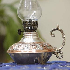 Pode incluir: Uma l&acirc;mpada de &oacute;leo de prata e cobre com uma chamin&eacute; de vidro e uma al&ccedil;a decorativa. A l&acirc;mpada tem um design ornamentado e &eacute; perfeita para adicionar um toque de charme vintage a qualquer casa.
