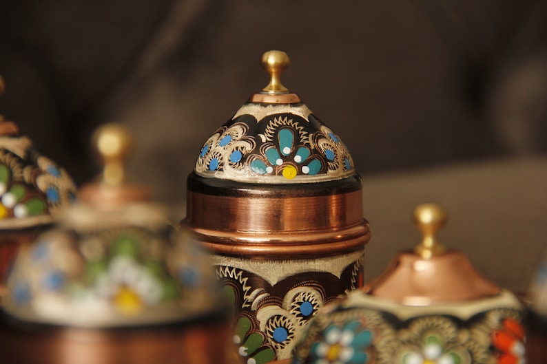 Pode incluir: Conjunto de quatro recipientes de cobre com desenhos pintados ornamentados em tons de azul, verde, branco e dourado. Os recipientes t&ecirc;m tampas abobadadas com remates.