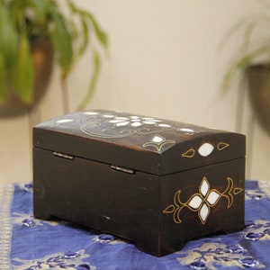 May include: A small, black wooden box with intricate gold and white inlay designs. The box has a hinged lid and is decorated with floral patterns.