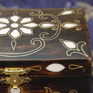 May include: A wooden box with a hinged lid and a brass latch. The box is decorated with a floral design and inlaid with mother-of-pearl.