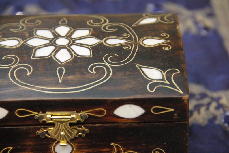 May include: A wooden box with a hinged lid and a brass latch. The box is decorated with a floral design and inlaid with mother-of-pearl.