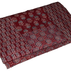 Op de afbeelding: Een bordeauxrode kantha-deken met een wit en blauw bloemenpatroon. De deken is dubbelgevouwen en heeft een textuur.
