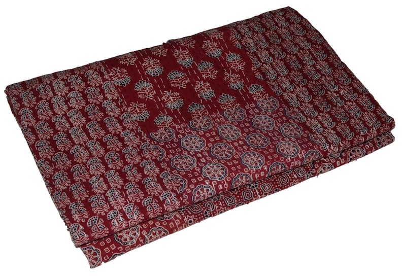 Op de afbeelding: Een bordeauxrode kantha-deken met een wit en blauw bloemenpatroon. De deken is dubbelgevouwen en heeft een textuur.