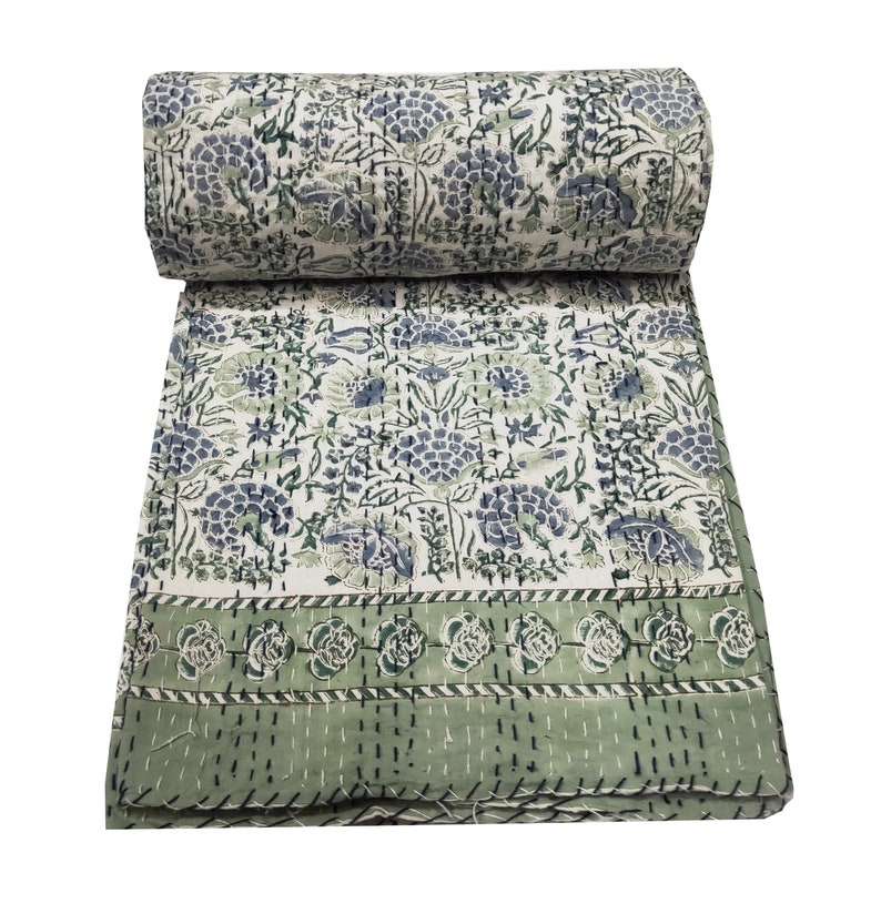 May include: A white and green kantha quilt with a floral pattern. The quilt is folded in half and has a green border.