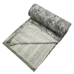 May include: A white and green kantha quilt with a floral print. The quilt is folded in half and rolled up, with the floral side facing out.