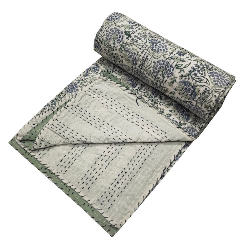 May include: A white and green kantha quilt with a floral print. The quilt is folded in half and rolled up, with the floral side facing out.