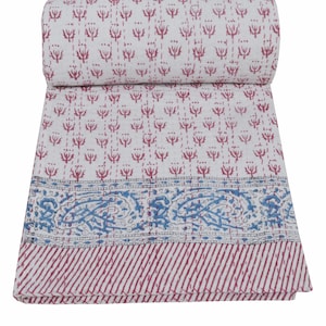 Könnte beinhalten: Eine weiße und rot gemusterte Steppdecke, oben aufgerollt. Die Steppdecke hat ein sich wiederholendes Blumendesign in Rot mit einem blau-weißen Rand. Der untere Rand hat rot-weiße Streifen.