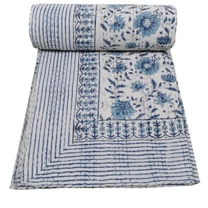 Può includere: Un trapunta di cotone bianco con un motivo floreale blu. La trapunta ha un bordo di strisce blu e un disegno floreale.