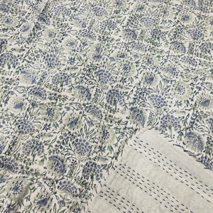 May include: A white kantha quilt with a floral pattern in shades of blue and green. The quilt is hand-stitched and has a subtle texture.