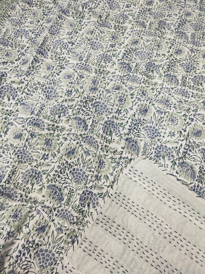 May include: A white kantha quilt with a floral pattern in shades of blue and green. The quilt is hand-stitched and has a subtle texture.