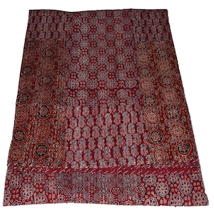 Op de afbeelding: Een rode kantha-deken met een patchwork-ontwerp met verschillende bloem- en geometrische patronen in tinten wit, zwart en blauw.
