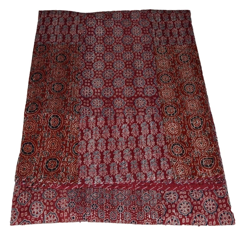 Op de afbeelding: Een rode kantha-deken met een patchwork-ontwerp met verschillende bloem- en geometrische patronen in tinten wit, zwart en blauw.