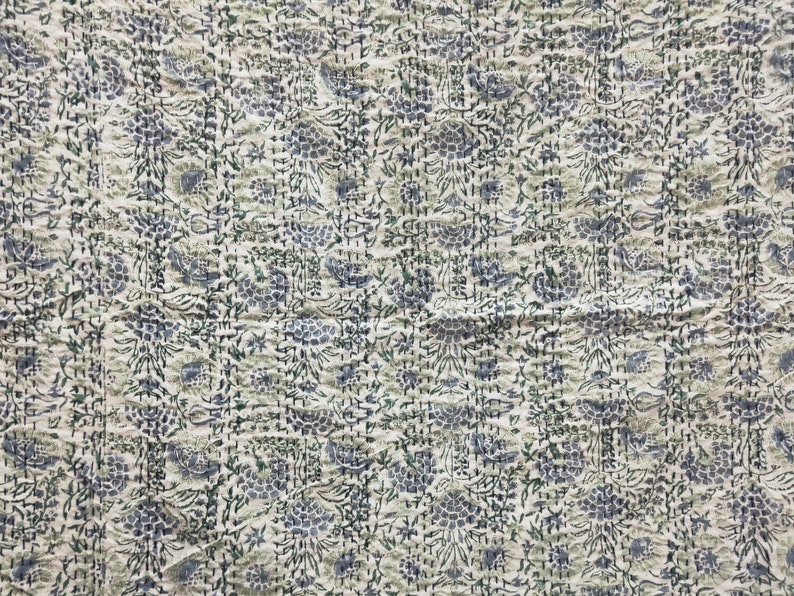 May include: A white cotton kantha quilt with a blue and green floral pattern. The quilt is hand-stitched and has a textured surface.