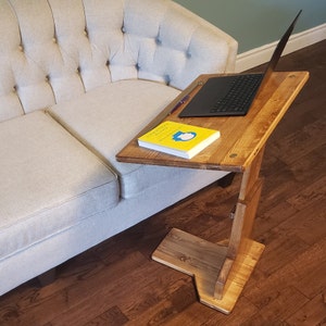 May include: A wooden side table with a laptop, pen, and book on top. The table is brown and has a unique design, with a base that slides under a sofa. The book has a yellow cover with the title "Cognitive".