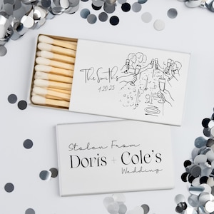 May include: White matchboxes with custom text and illustrations, perfect for weddings or events. One box is open, revealing the matchsticks. The text on the boxes reads "The Smiths" and "Stolen From Doris + Cole's Wedding."