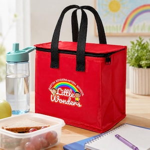 May include: A rectangular red insulated lunch bag with black fabric handles and a zipper closure. The front features a colorful graphic with a rainbow, two cartoon children, and the text "Austin Kindergarten School Little Wonders".