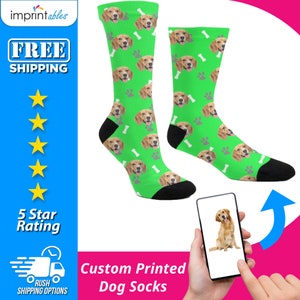 May include: A pair of green custom printed dog socks with a white bone and paw print pattern. The socks feature a dog's face repeated throughout the pattern. A smartphone is shown with a photo of a dog on the screen.