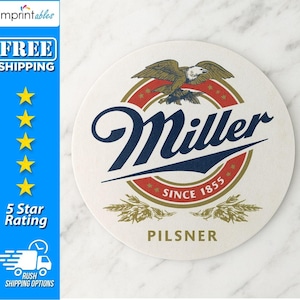 May include: A round, off-white coaster with the Miller logo. The logo features a navy blue script wordmark, a red and gold circular emblem with an eagle, and the text "SINCE 1855". The word "PILSNER" is printed at the bottom.