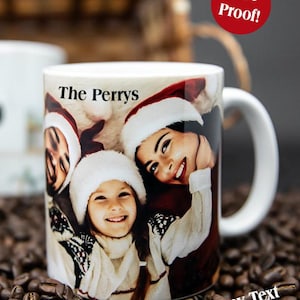 May include: A white ceramic mug featuring a printed photograph of a family wearing Santa hats, with the text The Perrys printed above the image and the text Add any Text or photo! printed at the bottom right of the mug.