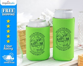 May include: Two green foam can coolers with a black and white graphic of a cabin in the woods with the text "Wild in the Woods" and "Jackie's Bach 2022".