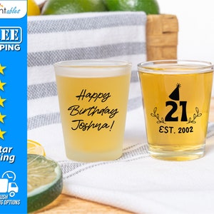 May include: Two clear shot glasses with black text. One glass says "Happy Birthday Joshua!" and the other says "21 EST. 2002" with a party hat graphic.