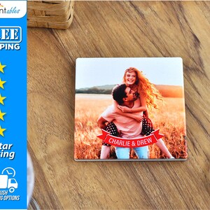 May include: A square ceramic coaster with a photo of a couple in a field. The man is carrying the woman on his back. They are both smiling. A red banner with the text "CHARLIE & DREW" is in front of them.
