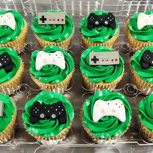 May include: A dozen green frosted cupcakes decorated with black and white video game controllers and NES controllers.