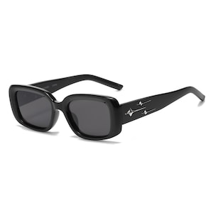 May include: Black rectangular sunglasses with dark lenses. The frames are thick and feature a starburst design on the temples. The sunglasses have a modern, retro aesthetic.