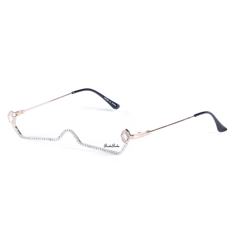 May include: Gold-tone metal glasses with a clear frame and rhinestones along the top edge. The glasses have a unique, wavy shape and feature a small, round, clear stone on each side.